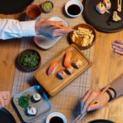 Diners sharing sushi, nigiri and Japanese small plates with chopsticks at a wooden table