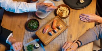 Diners sharing sushi, nigiri and Japanese small plates with chopsticks at a wooden table