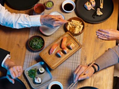 Diners sharing sushi, nigiri and Japanese small plates with chopsticks at a wooden table